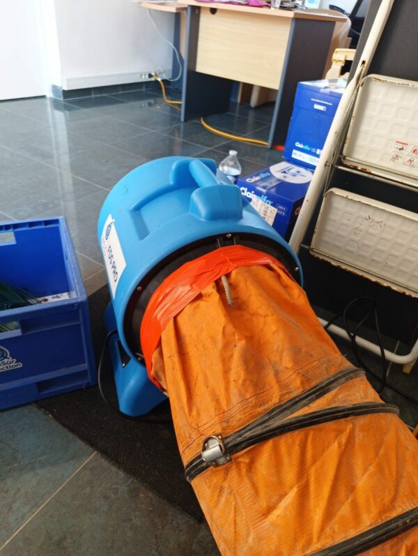 Raccordement d'un caisson de ventilation professionnel à une gaine de soufflage orange pour le traitement de l'humidité après un dégât des eaux.