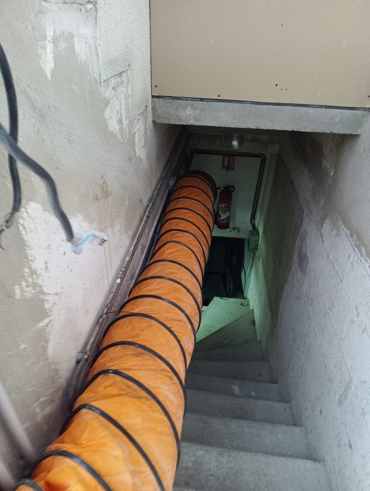 Déploiement vertical d'une gaine de séchage orange dans une cage d'escalier pour assainir et ventiler les sous-sols et caves humides.